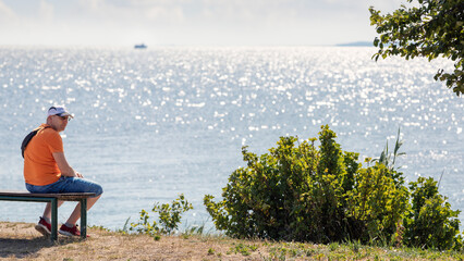 A man sits on a bench and rests, a beautiful view of the Curonian Lagoon with a boat in the...