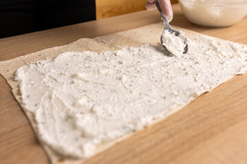 A layer of cheese filling is placed on the unfolded pita bread. Preparation of pita bread roll. © Vasyl