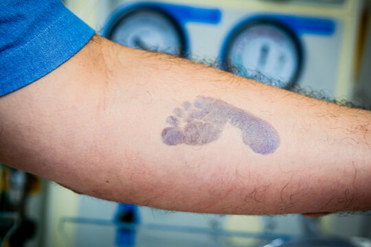 tatuagem do P&eacute; do beb&ecirc; rec&eacute;m-nascido no bra&ccedil;o do pai