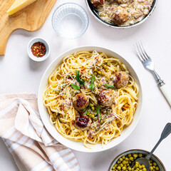 Spaghetti with meatballs and cream sauce is served on a plate with herbs and parmesan.