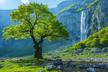 Fototapeta na wymiar A solitary tree stands before a towering waterfall amid lush greenery and jagged cliffs.
