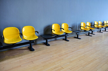 perspective view of empty yellow seats line on blue wall of waiting room