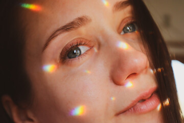 Portrait of a beautiful young white woman with blue eye and colorful light spots, reflections on face skin. Smiling girl has fun looking in camera.