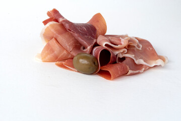 Slices of dry-cured pork ham with olives on a white background. Jamon delicacy.