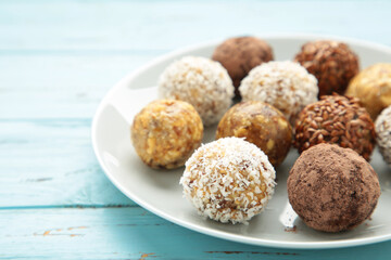 Healthy raw energy balls. Candy vegan balls of dates, nuts and coconut on plate on blue background. Top view, concept of useful home-made candies without sugar