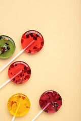 Fototapeta premium Colorful sweet lollipops with berries on beige background. Vertical photo