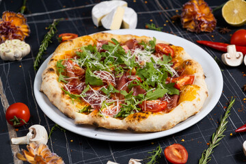 Baked pizza with salami, prosciutto and chicken with red sauce and melted cheese on a black wooden background in a composition with ingredients. Top view