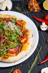 Baked pizza with salami, prosciutto and chicken with red sauce and melted cheese on a black wooden background in a composition with ingredients. Top view