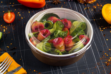 Salmon salad with green leaves, avocado and tomato on black stone background. Top view with copy space.