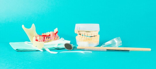 Tooth model, brushes, floss and dental tools on teal background with space for text.