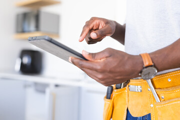 African American workman in tool belt interacts with a tablet
