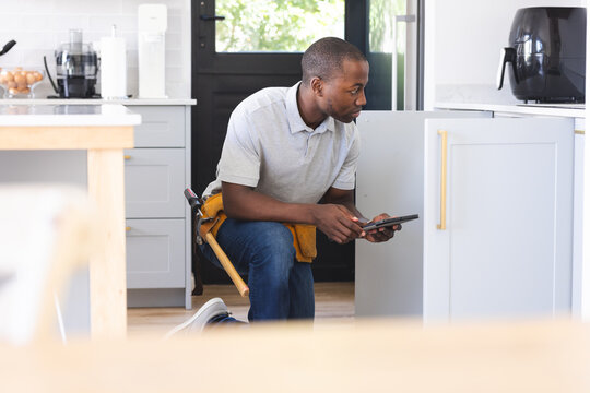 African American plumber fixing sink while using tablet - Powered by Adobe