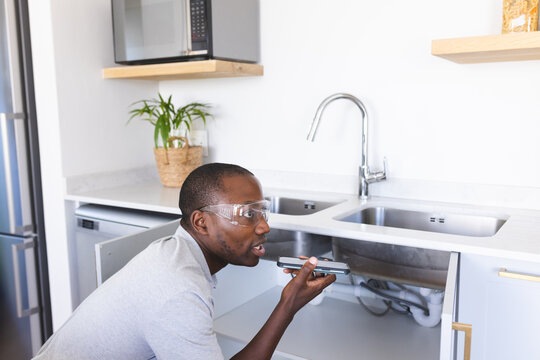 African American plumber fixing sink while making phone call - Powered by Adobe