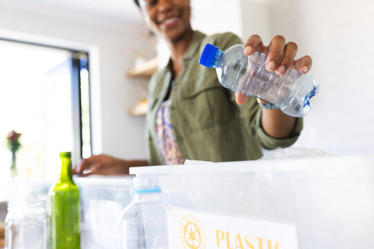A young African American woman sorts plastics into a recycling bin at home in the kitchen