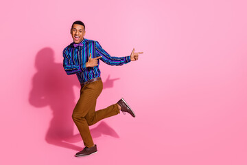 Fototapeta na wymiar Full length photo of cool excited guy wear striped shirt showing two fingers empty space isolated pink color background