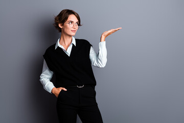 Photo of dreamy cute lady clerk dressed black vest eyewear looking showing arm empty space isolated grey color background - 763437727