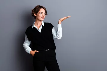 Papier Peint photo Échelle de hauteur Photo of dreamy cute lady clerk dressed black vest eyewear looking showing arm empty space isolated grey color background