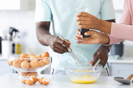 A diverse couple is preparing a meal together, making eggs, in a kitchen at home