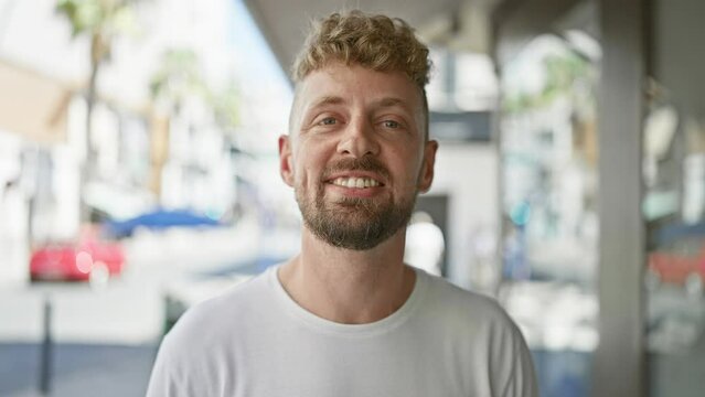 Portrait of a smiling young caucasian man with blue eyes and a beard standing on a city street.