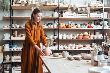 Handmade Craft: Woman with Earthenware in Pottery Shop. Young brunette potter with a serene expression showcasing her handmade vase in a pottery shop