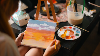 A person is painting with a palette of colors on a table. The table is covered with a floral...