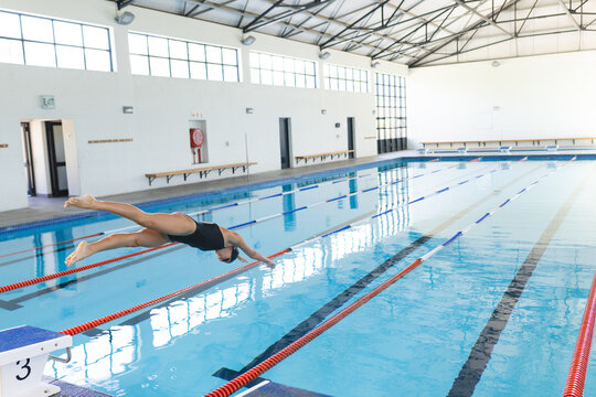 A Caucasian female athlete swimmer dives into a clear blue pool with copy space
