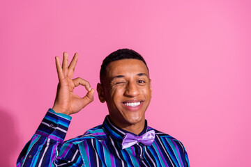 Photo of flirty funky guy dressed striped shirt showing okey sign winking eye empty space isolated...
