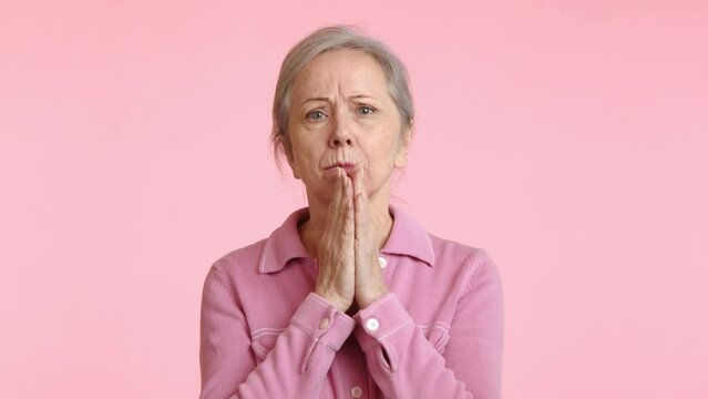 A senior woman shows an expression of astonishment, with wide eyes and hands on her cheeks, reacting to unexpected news or events. Camera 8K RAW. 
