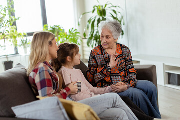 Generational bonding, grandmother, daughter, and grandchild sharing stories on a cozy afternoon - 763446972