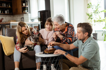 Joyous Family Celebrating Grandmothers Birthday With Cake in a Cozy Living Room - 763447101