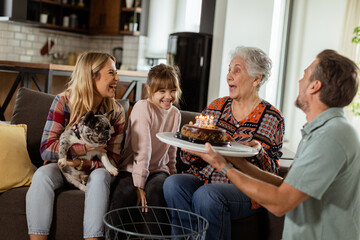 Joyous Family Celebrating Grandmothers Birthday With Cake in a Cozy Living Room - 763447106