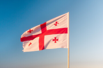 The flag of Georgia flutters in the wind against the blue sky. Georgian flag on the sky.