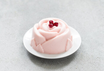 Pomegranate cream dessert, Panna Cotta in the shape of a rose. Decorated with pomegranate seeds. On a plate. Close-up