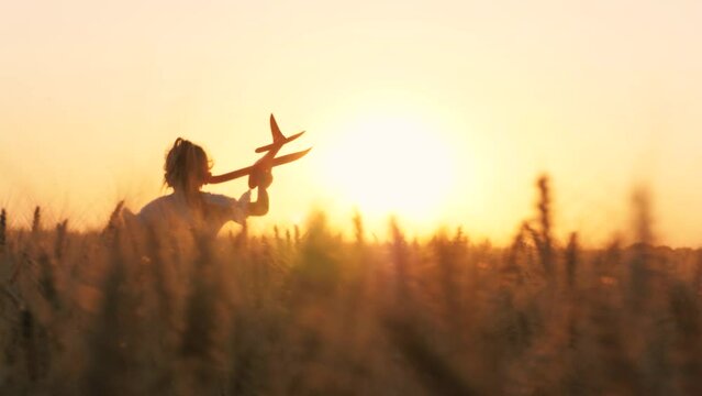 Cute little girl child running with plane toy playing at sunset sunrise wheat field happy childhood back view. Adorable female kid flying aircraft plaything pilot imagination fantasy enjoy freedom