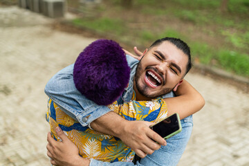 Top view image of two smiling gay friends greeting each other with a big hug in the open air. 