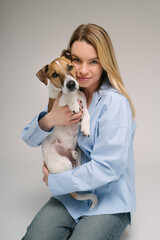 Woman hugging dog portrait. Adorable friends studio portrait. Blonde girl holding her pet Jack Russell terrier, sitting on the floor in photo studio