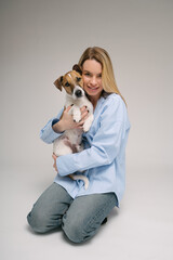 Woman hugging dog. Adorable friends studio portrait. Blonde girl holding her pet Jack Russell terrier, sitting on the floor in photo studio