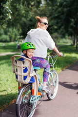 Smiling happy family enjoy riding bikes at Europe city streets on bright sunny day. Mom with children cycling at town park. Kid seating in safety baby chair bicycle. Healthy lifestyle activities