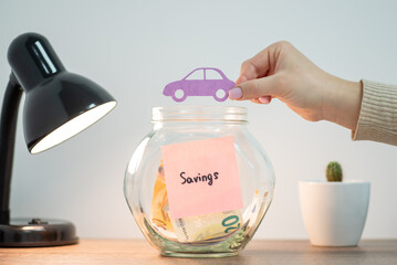 Hand with paper car over bank with euro money. Saving up money for a new car concept, buy vehicle