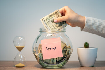 Woman putting dollar bills in glass jar. Saving money for a big purchase, taking part of salary for a dream