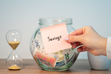 Jar with ukrainian hryvnia money in it. Female hand putting paper with inscription Savings. Saving up money for something in Ukraine