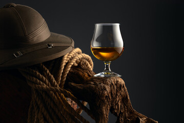 Snifter of brandy, cork tropical colonial helmet and rope on a old wooden snag.
