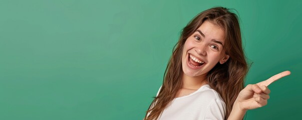 Cheerful brunette woman in white shirt pointing with excitement on a green background