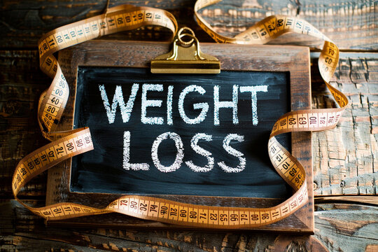A photo text of the Words " WEIGHT LOSS " written on chalkboard with measuring tape on wooden background.
