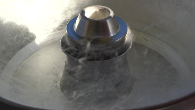 Close up of spinning machine for cotton candy. Preparing cotton candy in machine outdoors. Making cotton candy or candy floss in street food market. Molten raw sugar in household appliance.