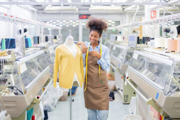 An American female designer points and stands next to a mannequin to design a garment made from woven fabric woven by machines running a large sewing factory, a global export industry. - obrazy, fototapety, plakaty