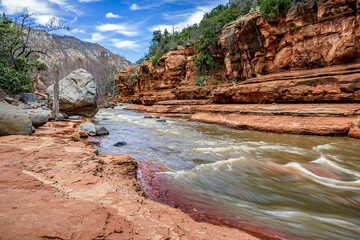 A large gray boulder sits next to Oak Creek in Arizona's red rock country - 763485542