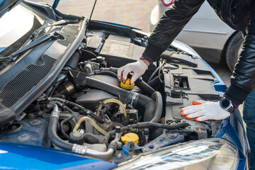 hands of a strong man in gloves inspect the car under the hood for damage.