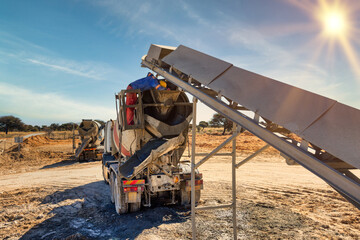 cement mixer truck, loaded by a conveyor belt, african worker on construction site at sunset, new...