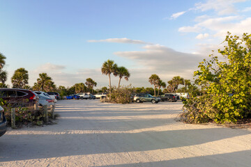Obraz premium Vehicle parking area with cars parked on ocean beach parking lot at sunset. Summer vacation on beachfront in Southern Florida